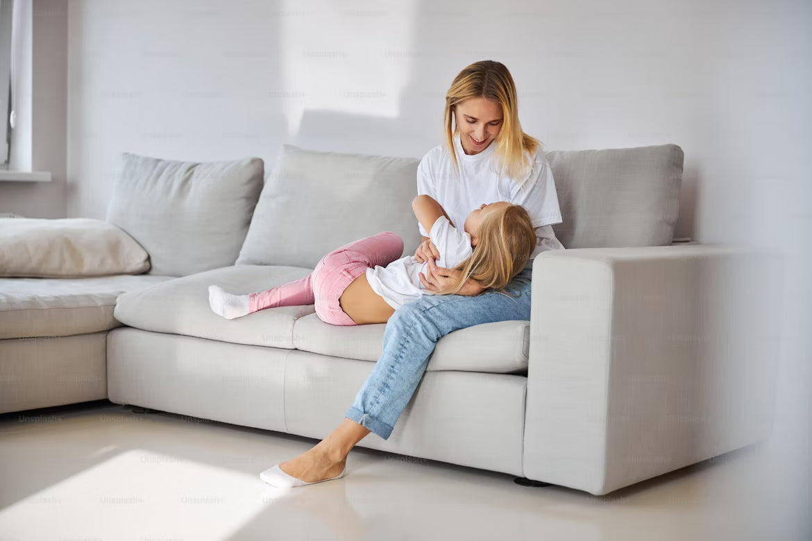 Woman and child sitting on a gray sofa in a bright living room.